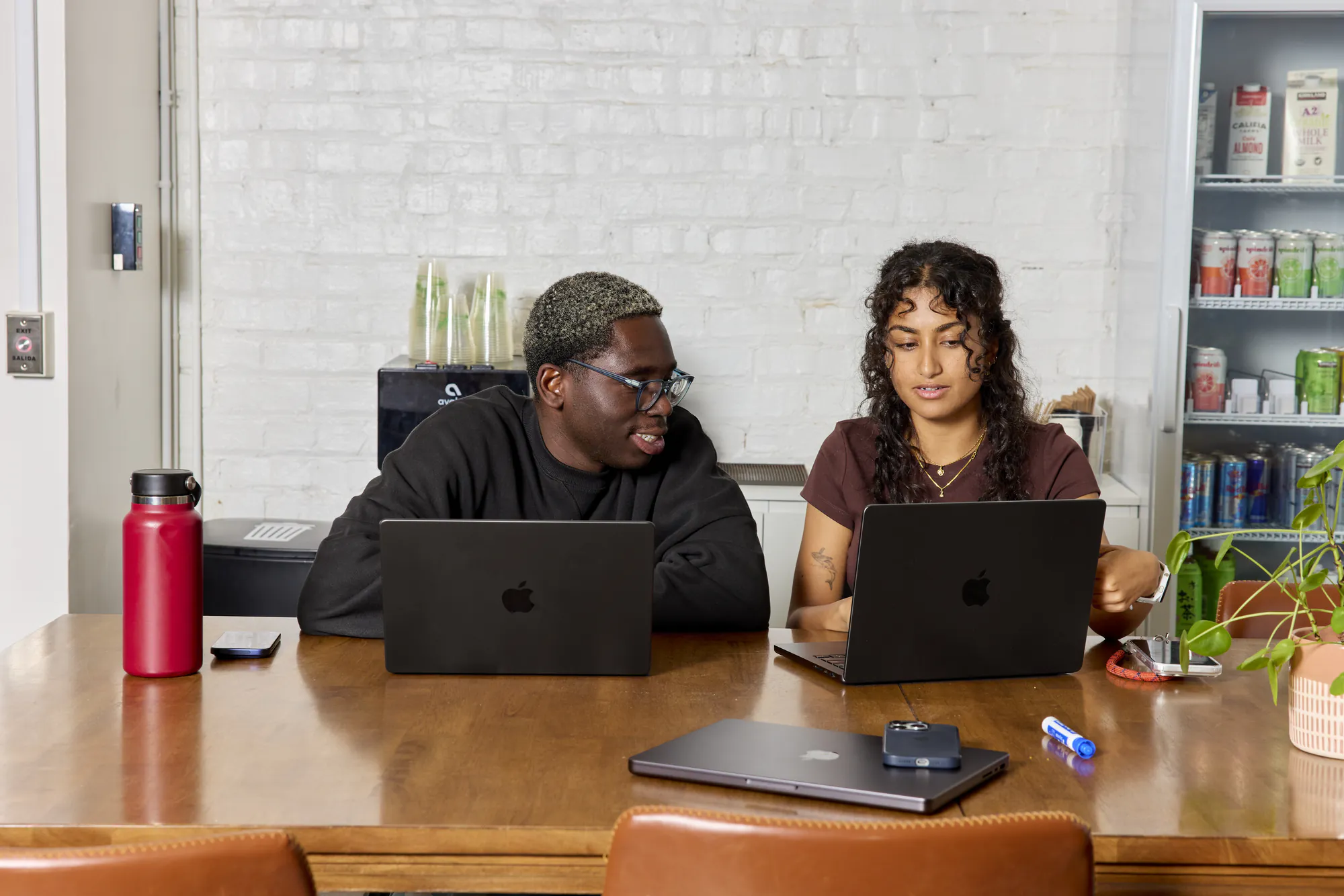 Two teammates working side by side on laptops at a shared table