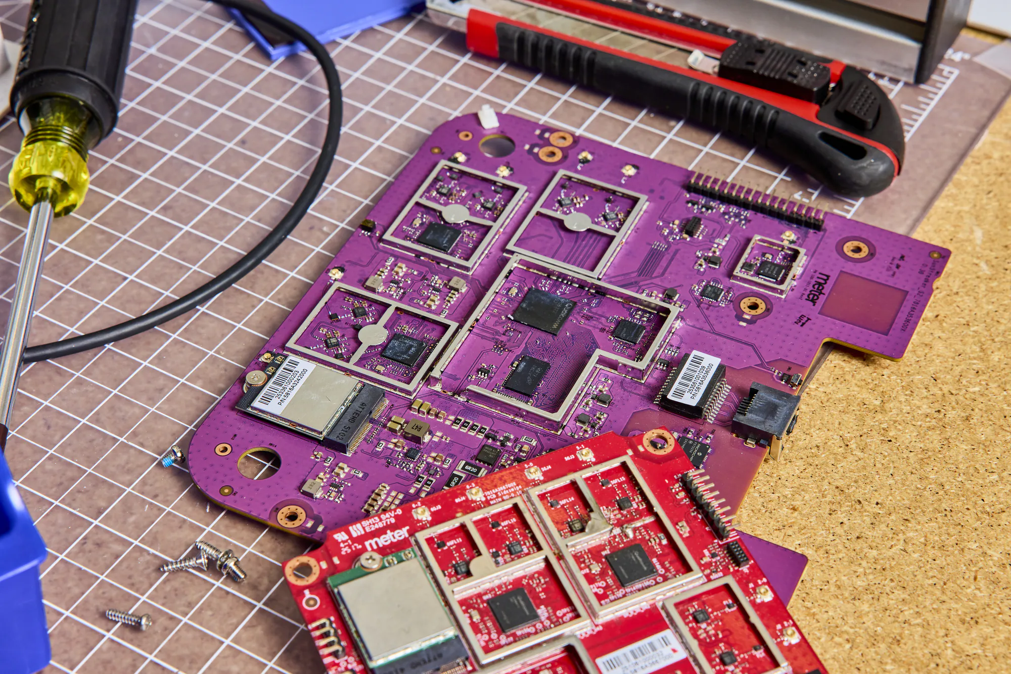Meter circuit boards (PVT and DVT) on a cutting mat beside a screwdriver